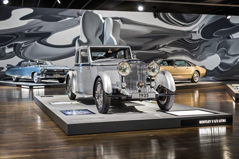 Bentley 3 1/2 Litre von 1935 in einer Autoausstellung Ein silberner Bentley 3 1/2 Litre Baujahr 1935 in einem modernen Ausstellungsraum, umgeben von weiteren klassischen Autos und einer abstrakten Wandkunst.